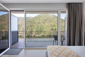 Un dormitorio con cama, un balcón con vistas a un paisaje montañoso y un comedor con sillas.