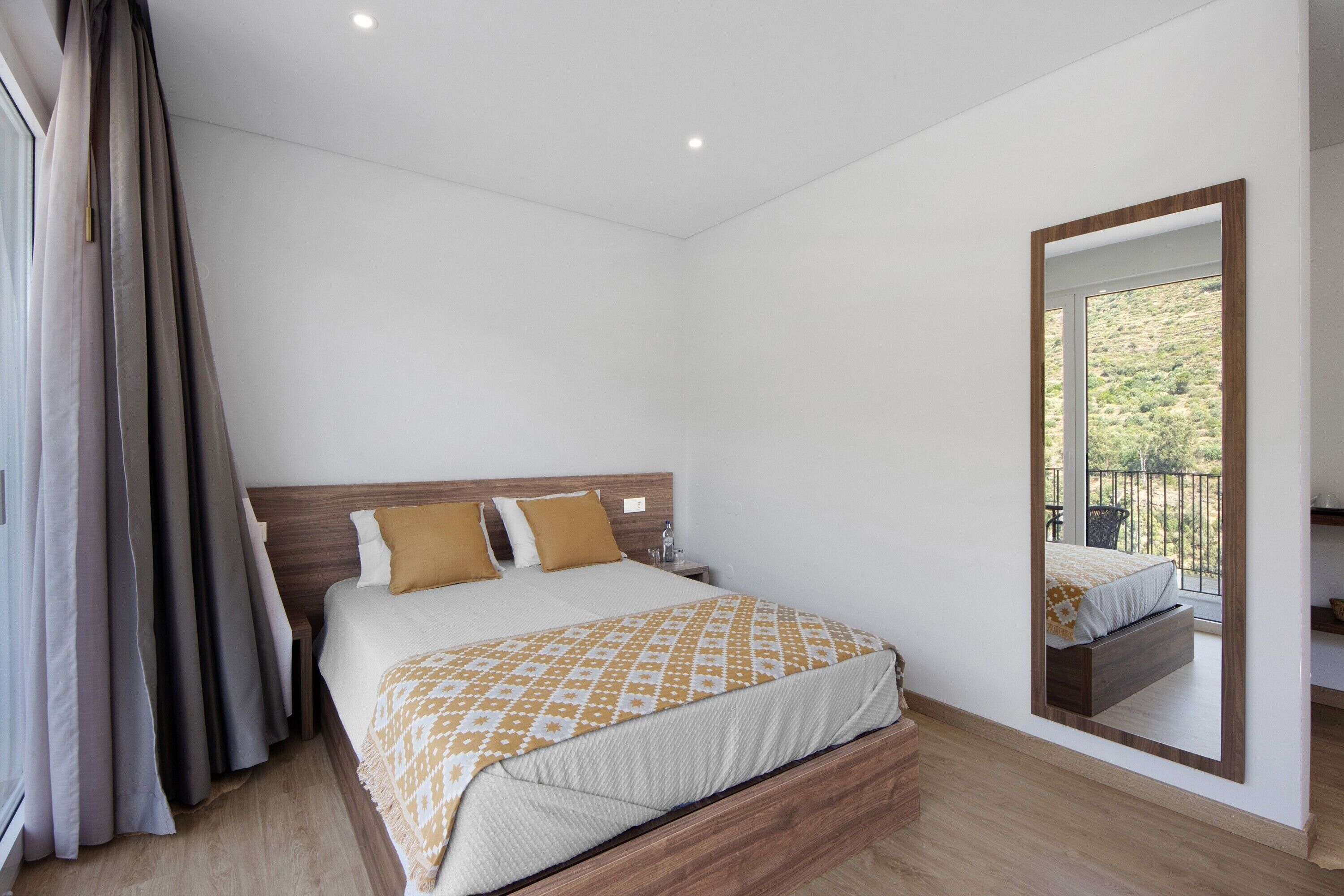 Een slaapkamer met een houten bed, een nachtkastje, een spiegel en uitzicht op een balkon.
