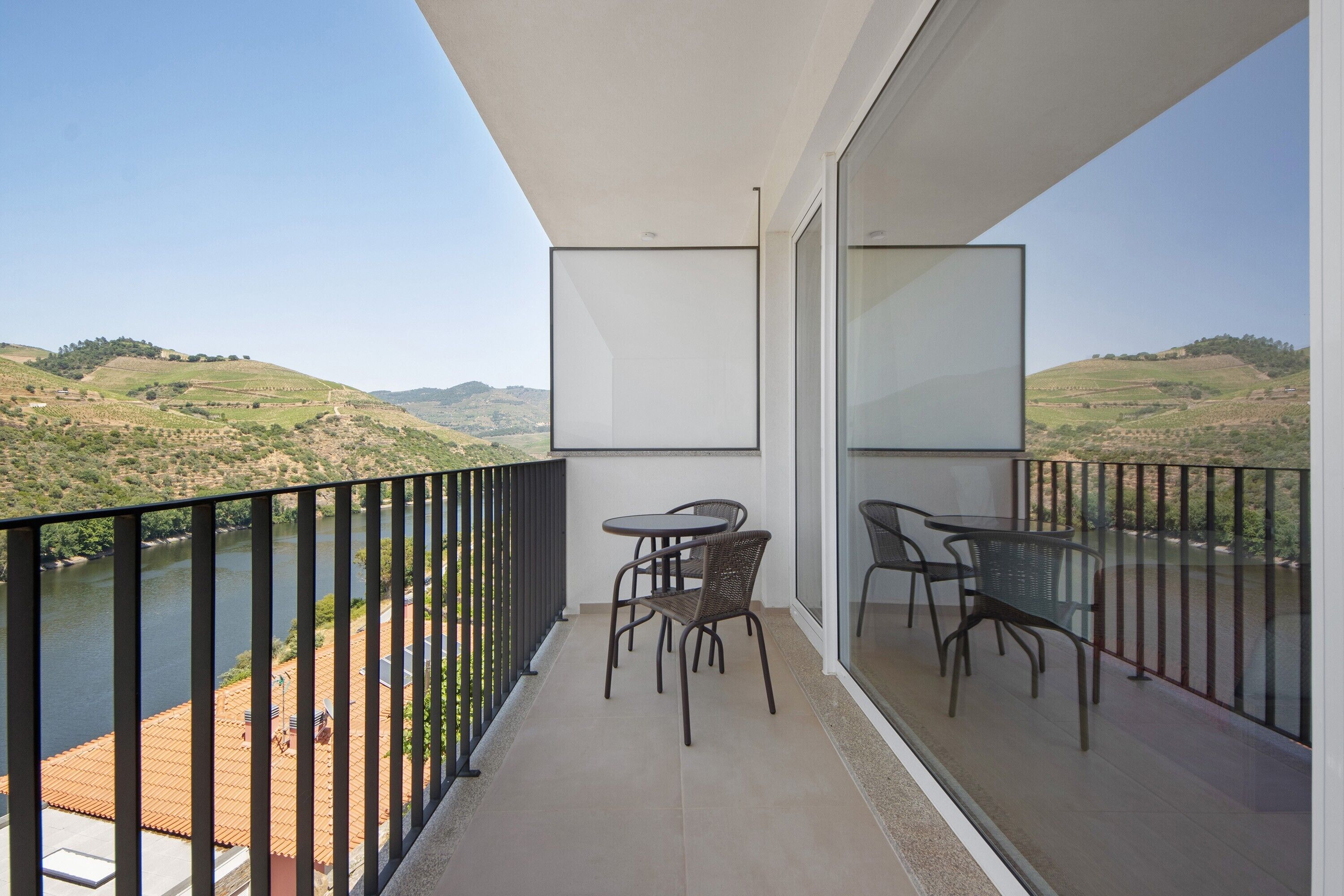 Un balcon donnant sur une rivière et des collines, aménagé avec deux tables et des chaises.