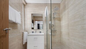 Une salle de bain moderne avec une douche à l’italienne en verre, un meuble-lavabo blanc et une porte en bois.