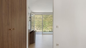 Un couloir avec une armoire en bois, un banc intégré et une grande porte-fenêtre coulissante donnant sur un balcon avec vue sur un paysage vallonné.