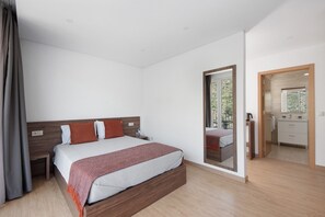 A modern hotel room with a large bed, a wooden headboard, a bedside table, and a bathroom visible through a glass door.