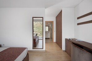 Une chambre avec un lit, un bureau en bois, un miroir et une vue sur un balcon.