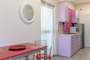 Una cucina compatta con un tavolo rosso, uno specchio con cornice bianca e un mobiletto viola con un forno a microonde.