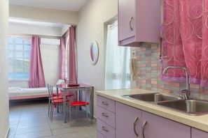 Una stanza compatta con un letto, un tavolino con sedie, un lavandino e una finestra con tende.