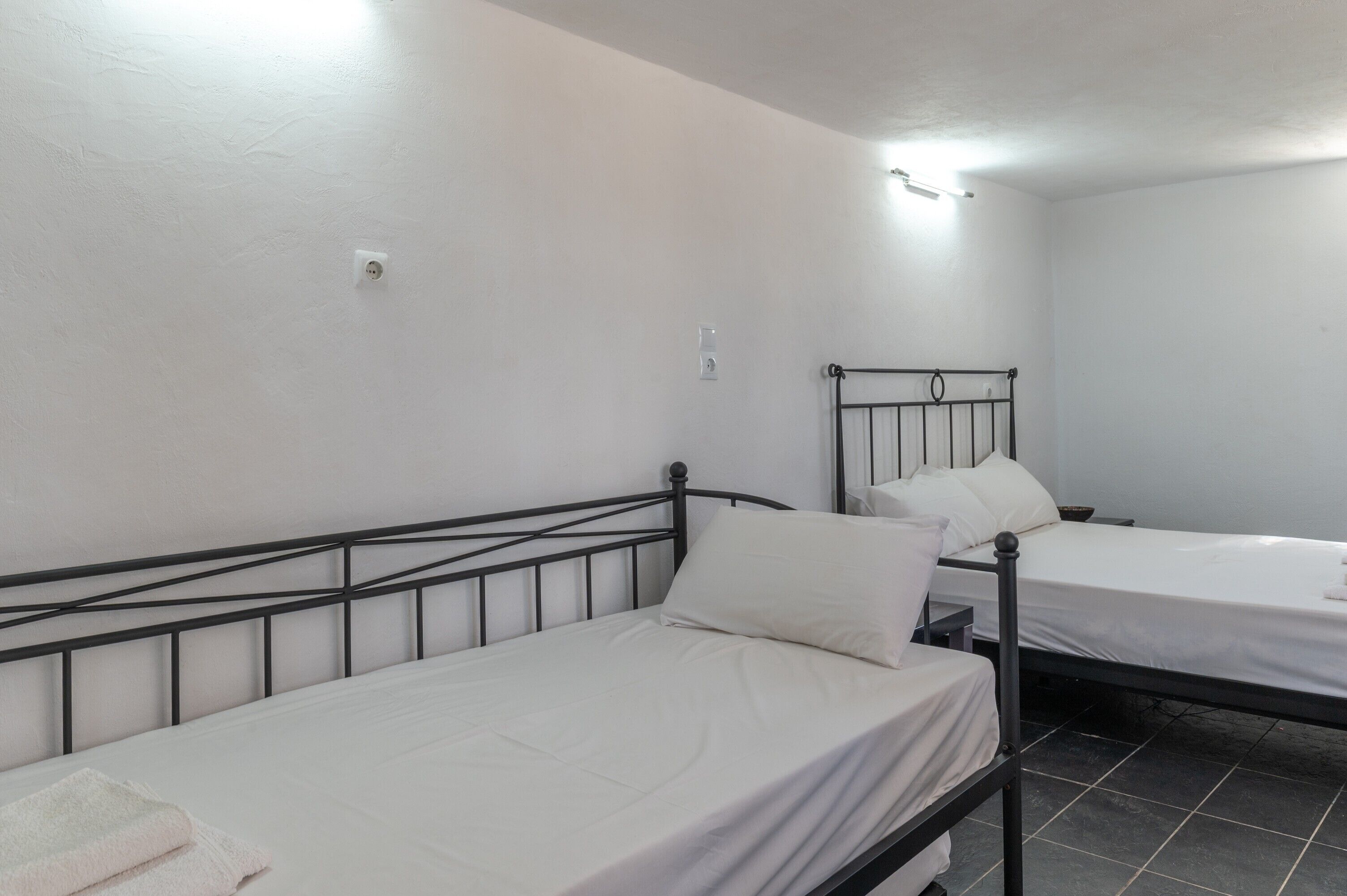 Duas camas de solteiro com estrutura de metal preto em um quarto com paredes brancas e piso de azulejos.