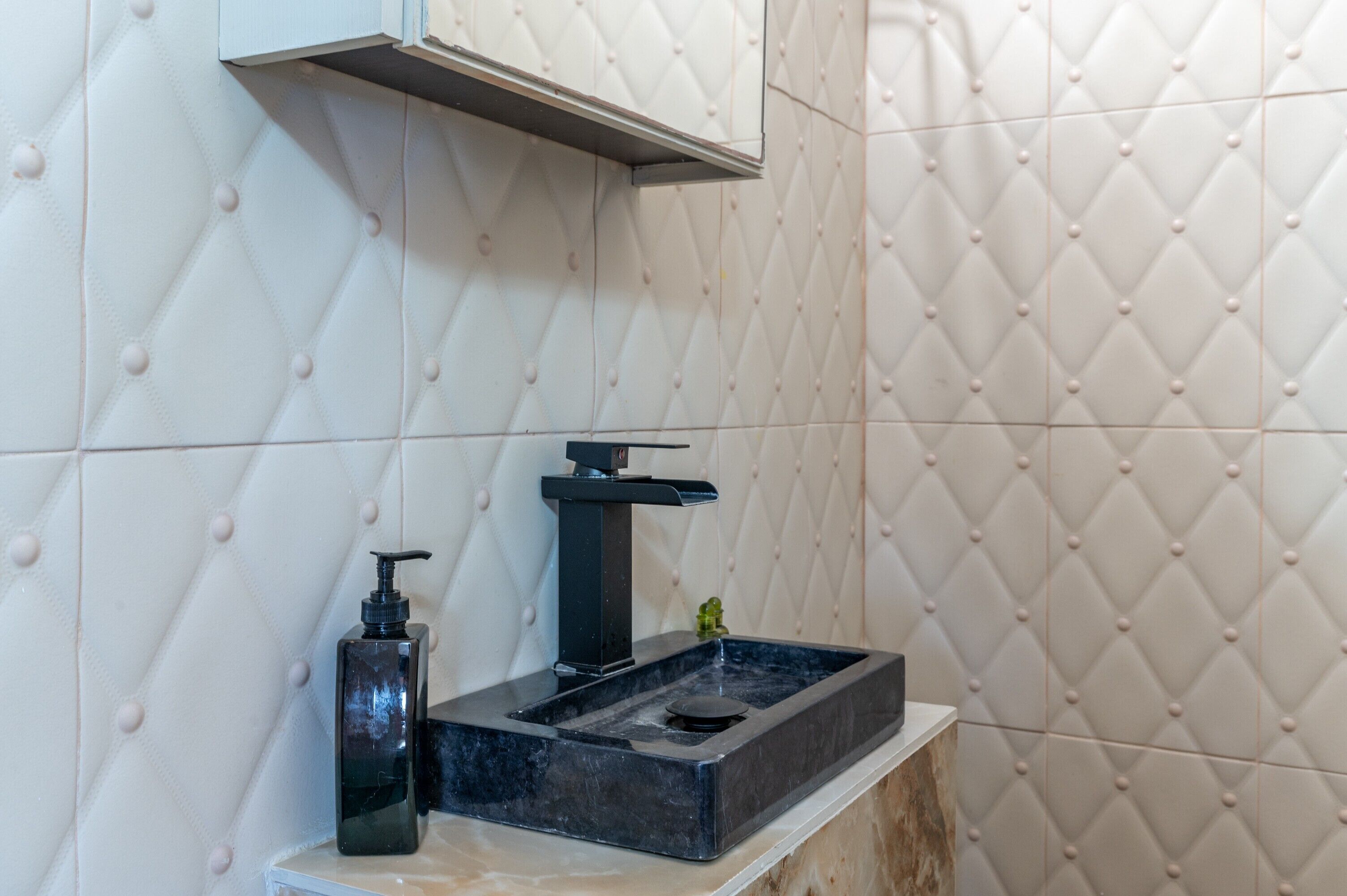 A bathroom with a marble sink, a black soap dispenser, and a white tiled wall with a diamond pattern.