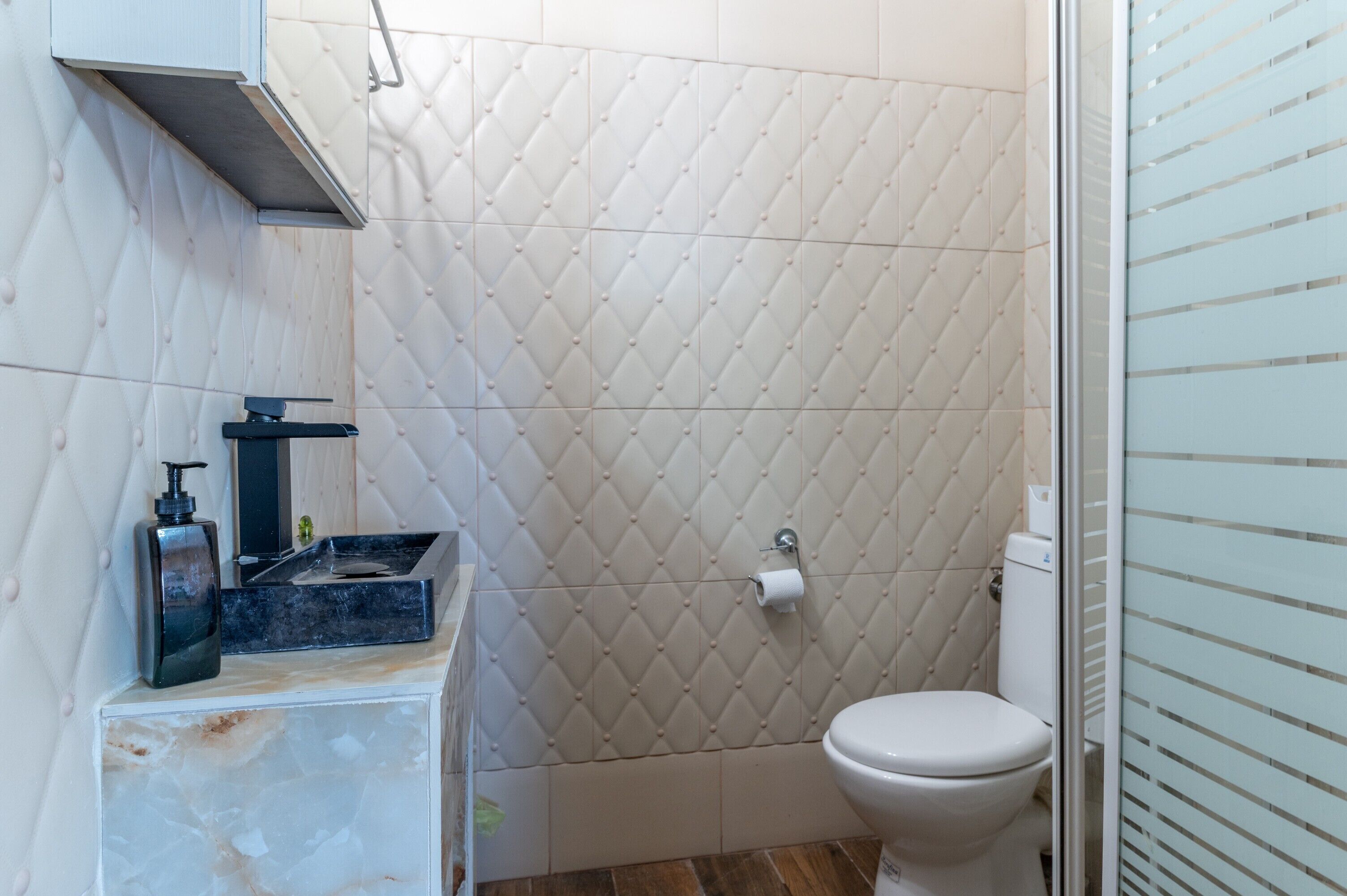 Un baño con un inodoro blanco, un lavabo con dispensador de jabón y un perchero para toallas.