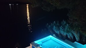 Ein Whirlpool mit blauem Licht, umgeben von einer weißen Struktur, in der Nähe von Wasser und Bäumen.