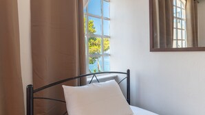 A bed with a white pillow, a window with curtains, and a mirror on the wall. - Apartment 'Artemis' with Sea View, Wi-Fi and Air Conditioning (Salamina)