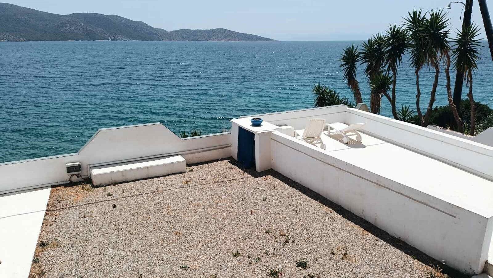 Une terrasse sur le toit offrant une vue sur la mer, avec une balustrade blanche et un petit espace salon.