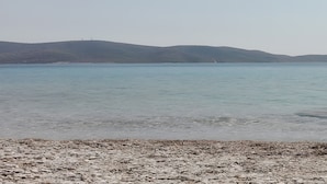 Un plan d’eau paisible, bordé d’une plage de galets et entouré de collines lointaines.