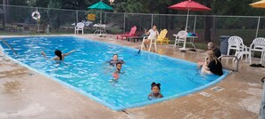 Una piscina con un puesto de salvavidas, sillas de descanso y sombrillas.