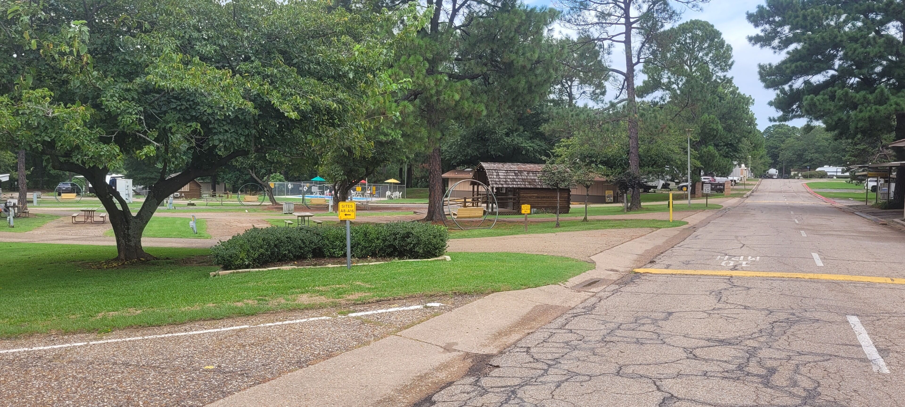 Ein Park mit Picknicktischen, einem Spielplatz und einem kleinen, hüttenartigen Gebäude.