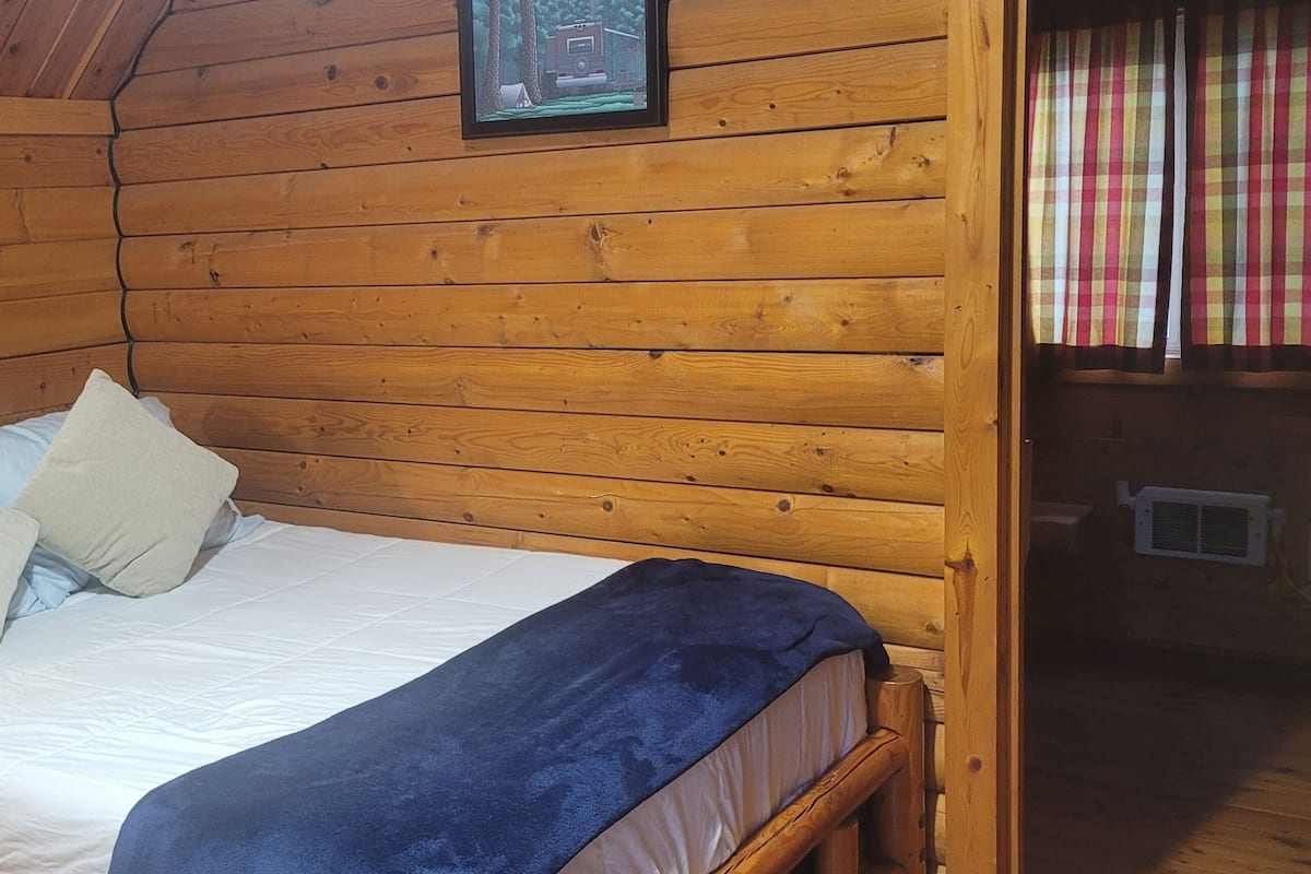 A wooden cabin bedroom with a bed, pillows, and a blue blanket.