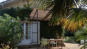 Ein Haus mit Schotterauffahrt, einem Holztisch und -stühlen draußen und einem Strohdach.