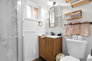 Une salle de bain avec une douche en marbre, un meuble-lavabo en bois, des toilettes blanches et un porte-serviettes.