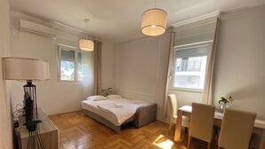 A bedroom with a bed, bedside table, lamp, and a desk with chairs.