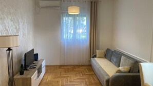 A modern living room with a sofa, a desk with a computer, a lamp, and an air conditioning unit.