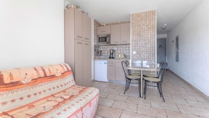 Un espace de vie compact comprenant un canapé, une table à manger avec des chaises, un coin cuisine et un mur recouvert de carreaux.
