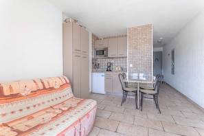 A compact living space with a sofa, a dining table with chairs, a kitchenette, and a tiled backsplash.