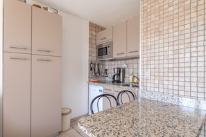 A kitchen with cabinets, a microwave, a coffee maker, and a tiled backsplash.