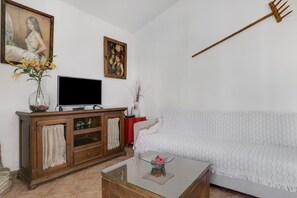 A living room with a sofa, a glass coffee table, a wooden cabinet, a television, and a painting on the wall.