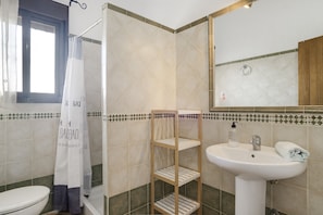 A bathroom with a toilet, shower, sink, and a mirror.