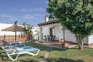 A patio with lounge chairs, a table, and a thatched roof structure.