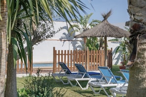 A beachside lounge area with sun loungers, a thatched umbrella, and a wooden fence.