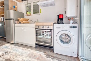 A compact kitchen with a stainless steel refrigerator, a built-in oven, a washing machine, and a coffee maker.
