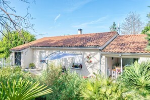 A house with a tiled roof, a covered porch, and a garden with various plants.