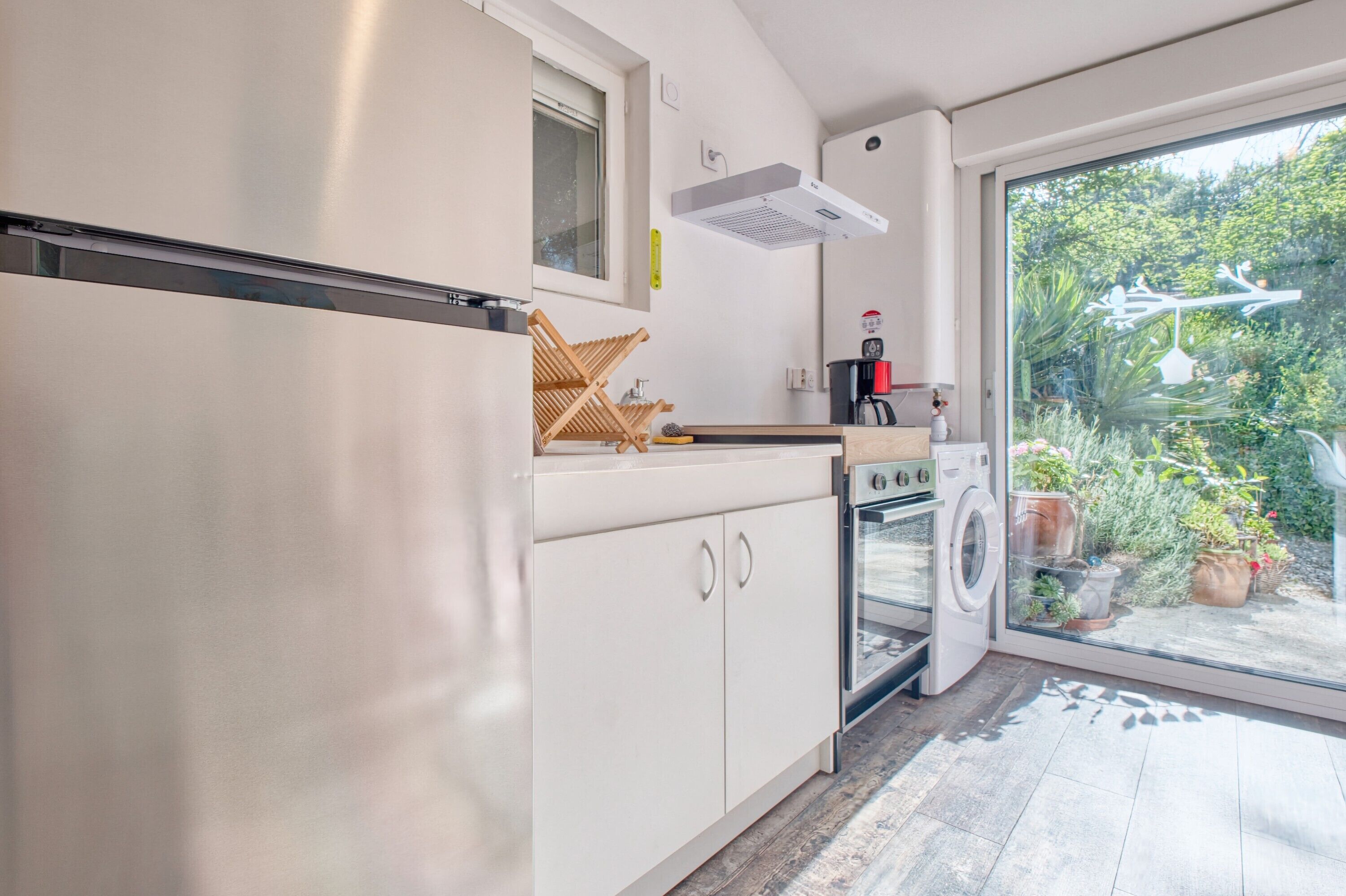 Cocina moderna con horno empotrado, lavadora y ventana grande con vistas a un jardín.