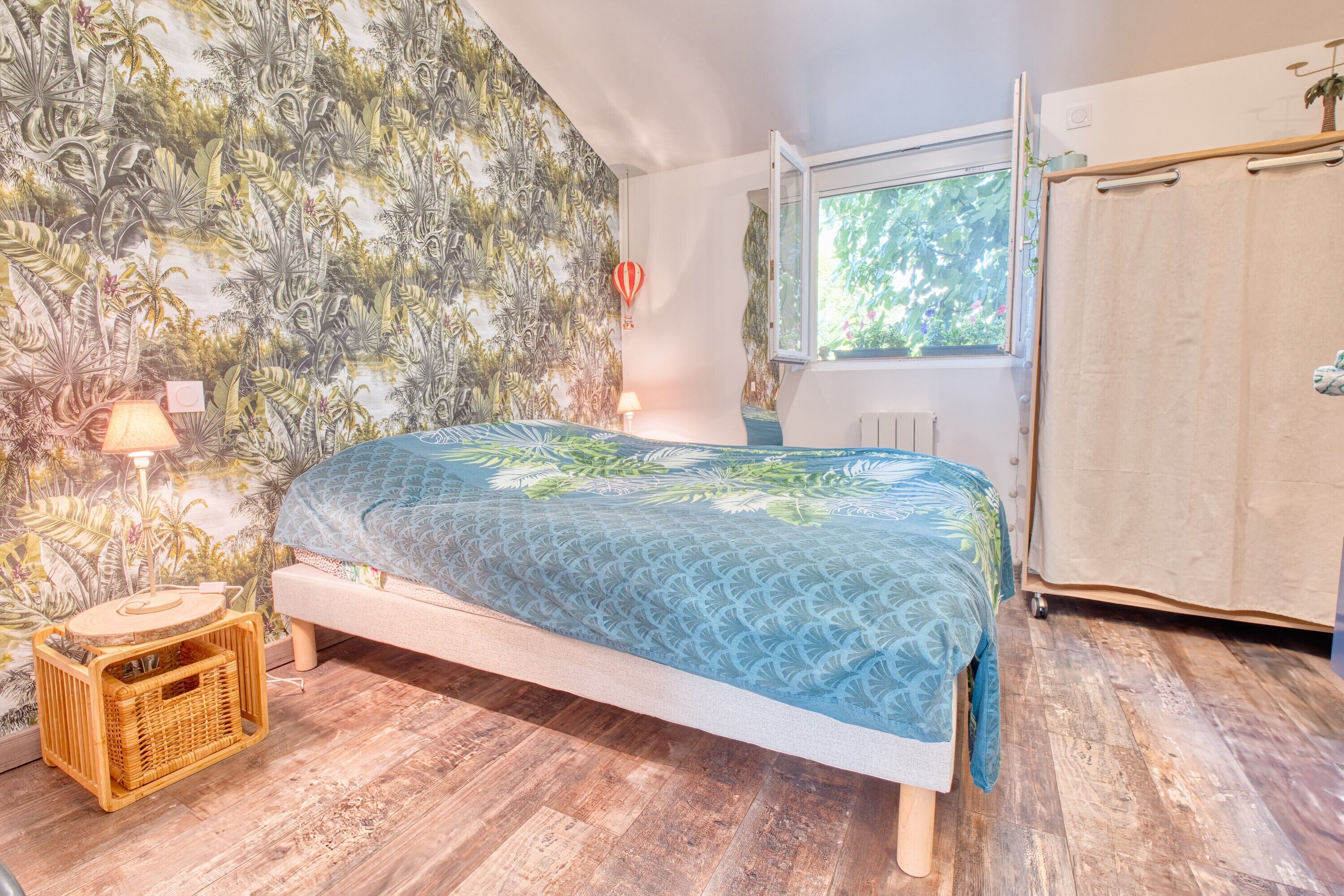 Une chambre avec un lit, une fenêtre, une armoire et un mur décoré sur le thème des tropiques.