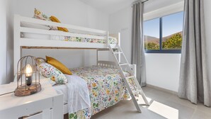 Une chambre avec un lit superposé, une échelle, un bureau avec une lampe et une fenêtre avec des rideaux.