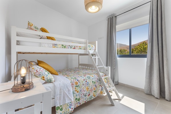 A bunk bed room with a ladder, a desk with a lamp, and a window with curtains.