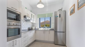 Une cuisine moderne dotée d’appareils électroménagers en acier inoxydable, de meubles blancs et d’une fenêtre offrant une vue sur les montagnes.