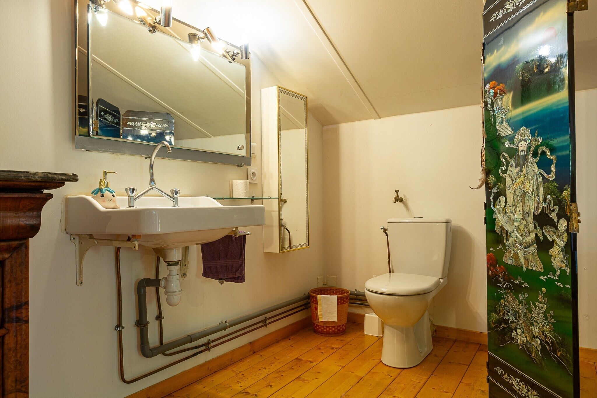 A bathroom with a sink, mirror, toilet, and a decorative painting.