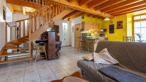 A wooden staircase leading to a loft, a kitchen with bar stools, and a sofa in a bright room. - Le Bacci Country House with Mountain View, Private Garden & Wi-Fi (Vals-les-Bains)
