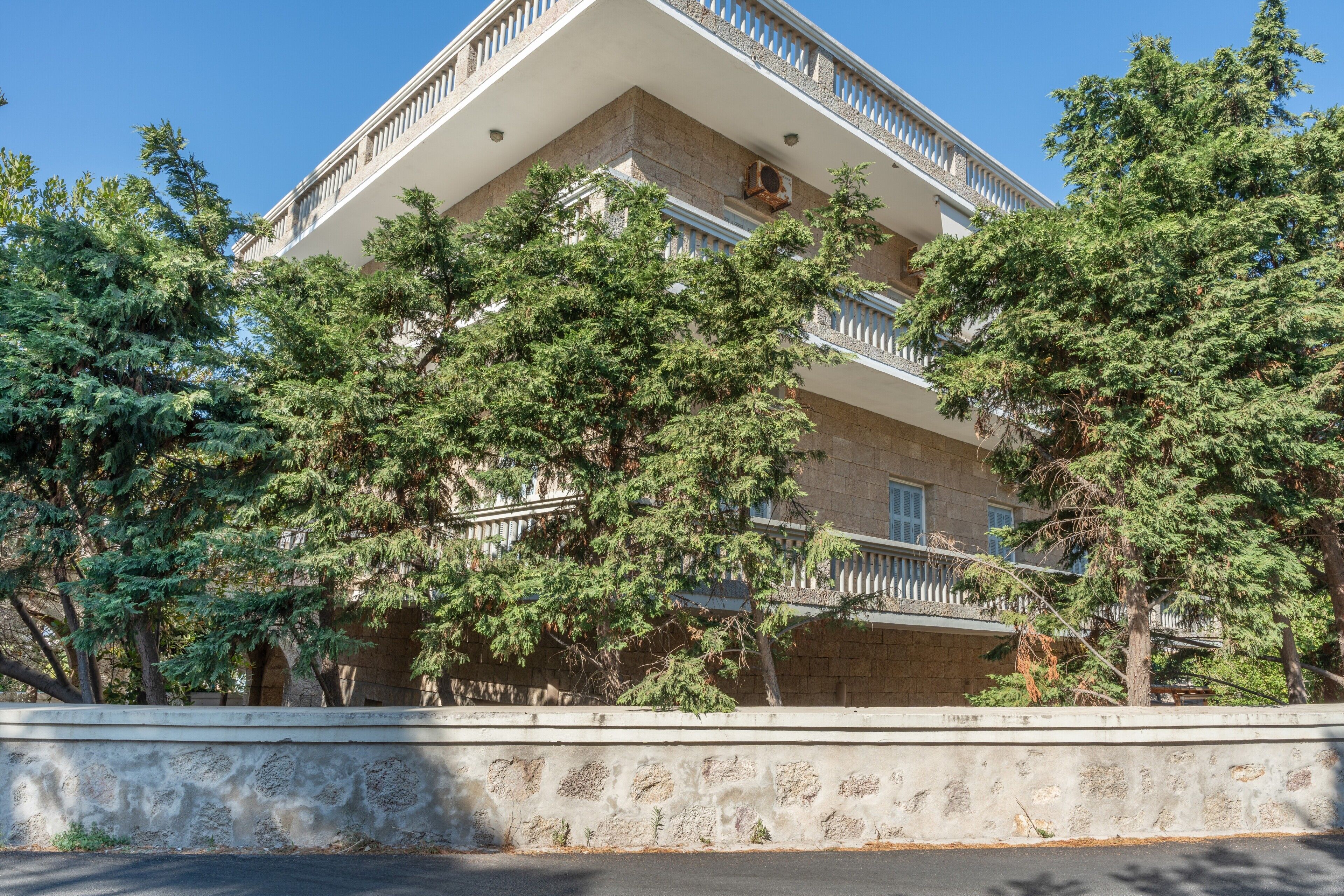 Un immeuble à plusieurs étages doté de balcons, entouré d’arbres.