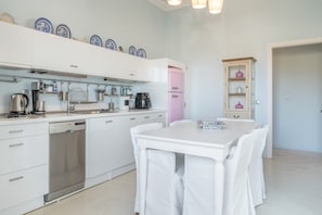 Moderni keittiö, jossa on valkoiset kaapit, vaaleanpunainen jääkaappi ja ruokailutila, jossa on valkoiset tuolit.