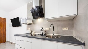 A modern kitchen with white cabinets, a stainless steel sink, a black countertop, and a flat-screen TV mounted above the microwave. - Casa Inés rural: 1 habitación, vistas a la montaña, Wi-Fi y aire acondicionado (Fernán Pérez)