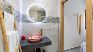 A bathroom with a round mirror, a sink with a decorative bowl, a towel rack, and a shower area. - Casa Inés rural: 1 habitación, vistas a la montaña, Wi-Fi y aire acondicionado (Fernán Pérez)