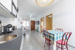 Una cocina moderna con microondas integrado, cafetera y un lavabo. Hay una zona de comedor con una mesa y sillas, además de un ventilador de techo.