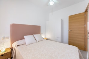 Un dormitorio con cama, mesita de noche, armario y ventilador de techo.