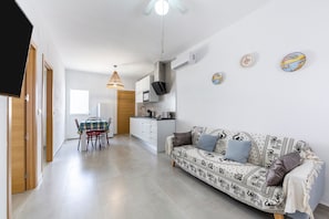 Una sala de estar moderna con un sofá, una mesa de comedor con sillas, una zona de cocina y un televisor montado en la pared.