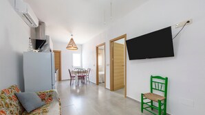 Una sala de estar moderna con un sofá, un sillón verde, un televisor de pantalla plana montado en la pared y una zona de comedor al fondo.