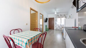 Un comedor con mesa y sillas, una cocina con pileta y encimera, y un televisor montado en la pared.