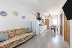 Een moderne keuken met witte kasten, een zithoek met tafel en stoelen, en een bank met een bloemenprint.