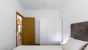 Un dormitorio con cama, una puerta de madera, un armario blanco y una lámpara colgante.